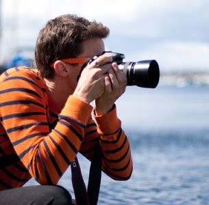 Man in stripped shirt taking photo with a camera without proper neck strap usage